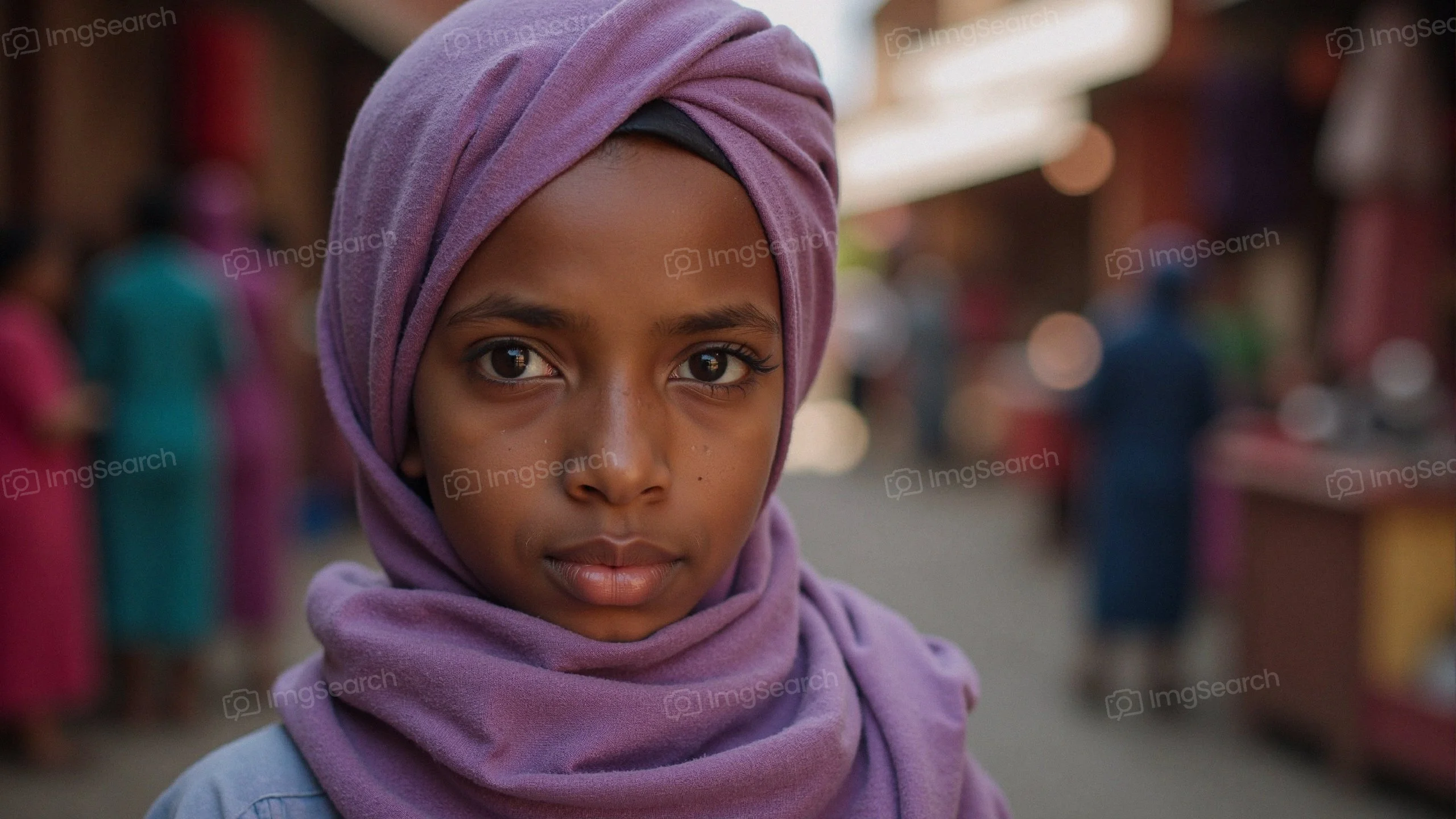 A portrait of a young girl wearing a purple headscarf in a colorful market.