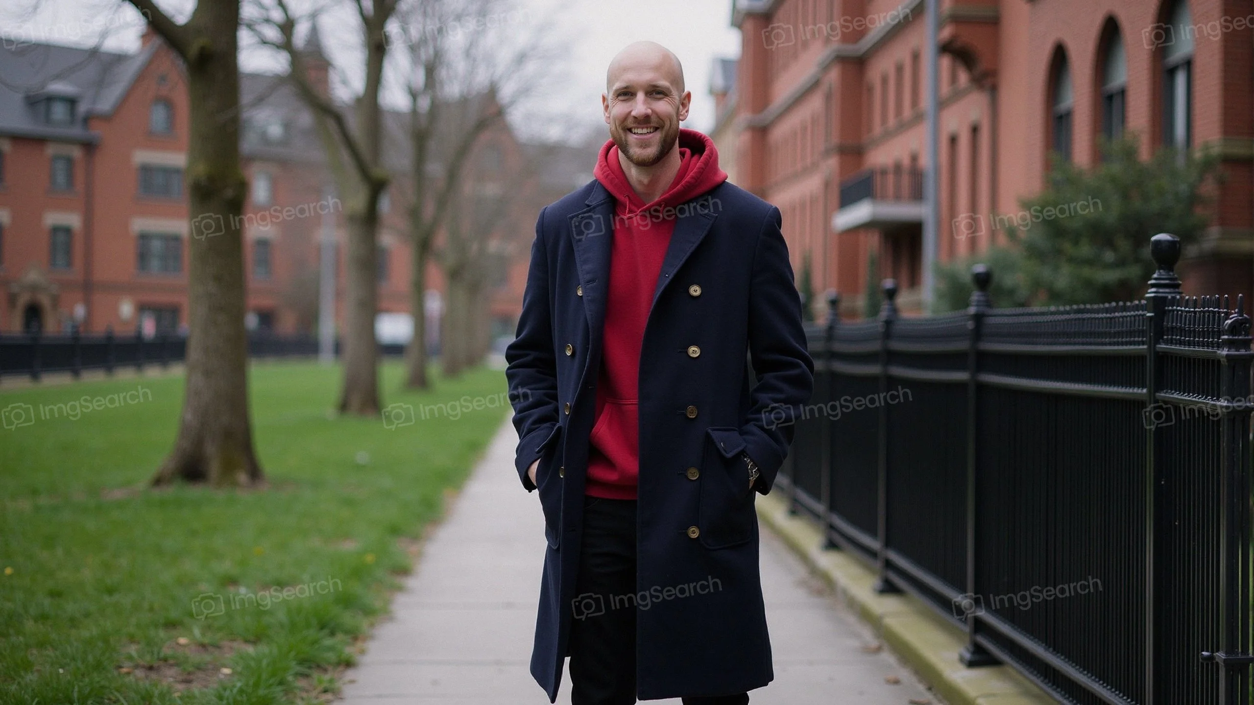 Man wearing a navy overcoat red hoodie standing on a city sidewalk