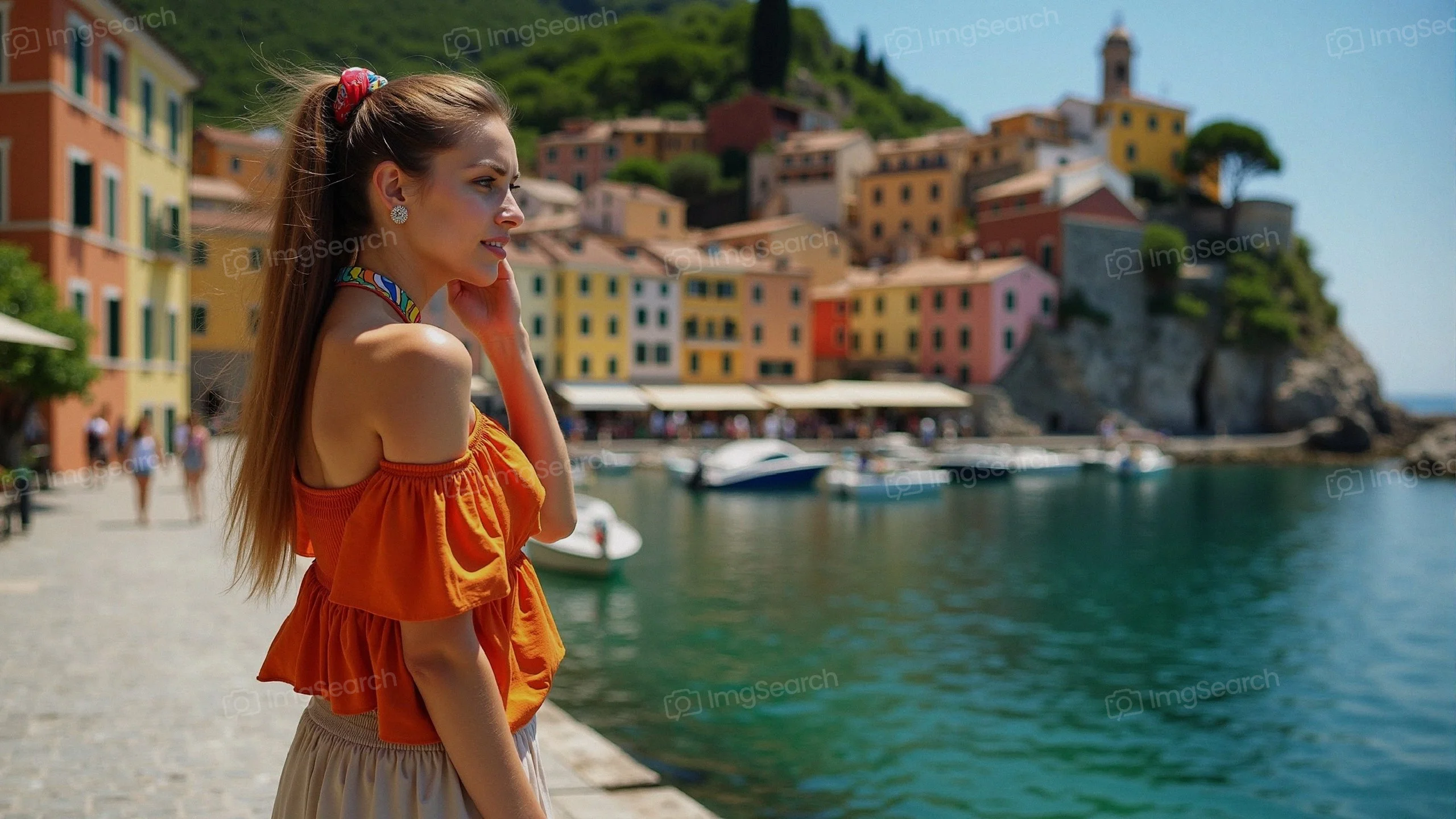 A young woman in an orange top standing by a waterfront with colorful buildings in the background.