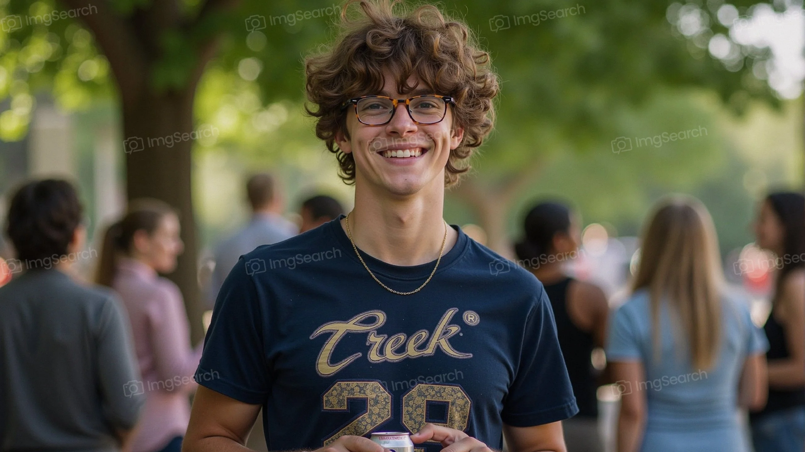 A young man with curly hair glasses smiling in a summer gathering.