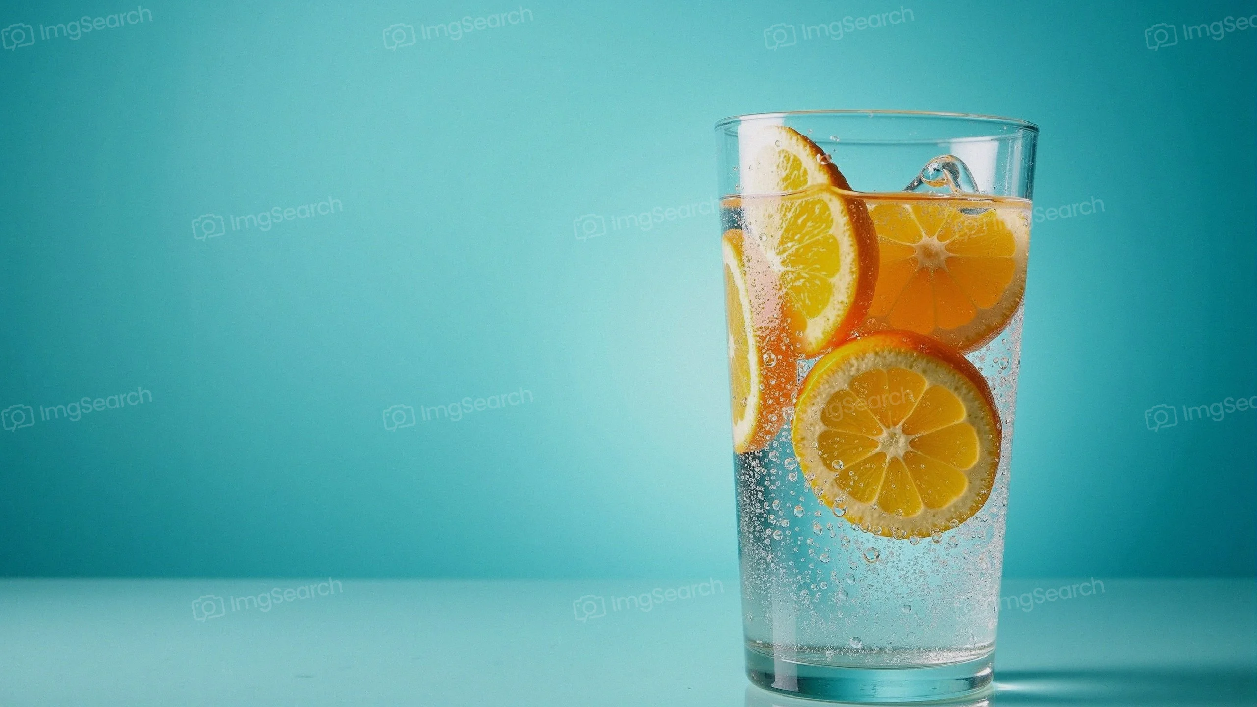 A glass of sparkling water with orange slices against a teal background.