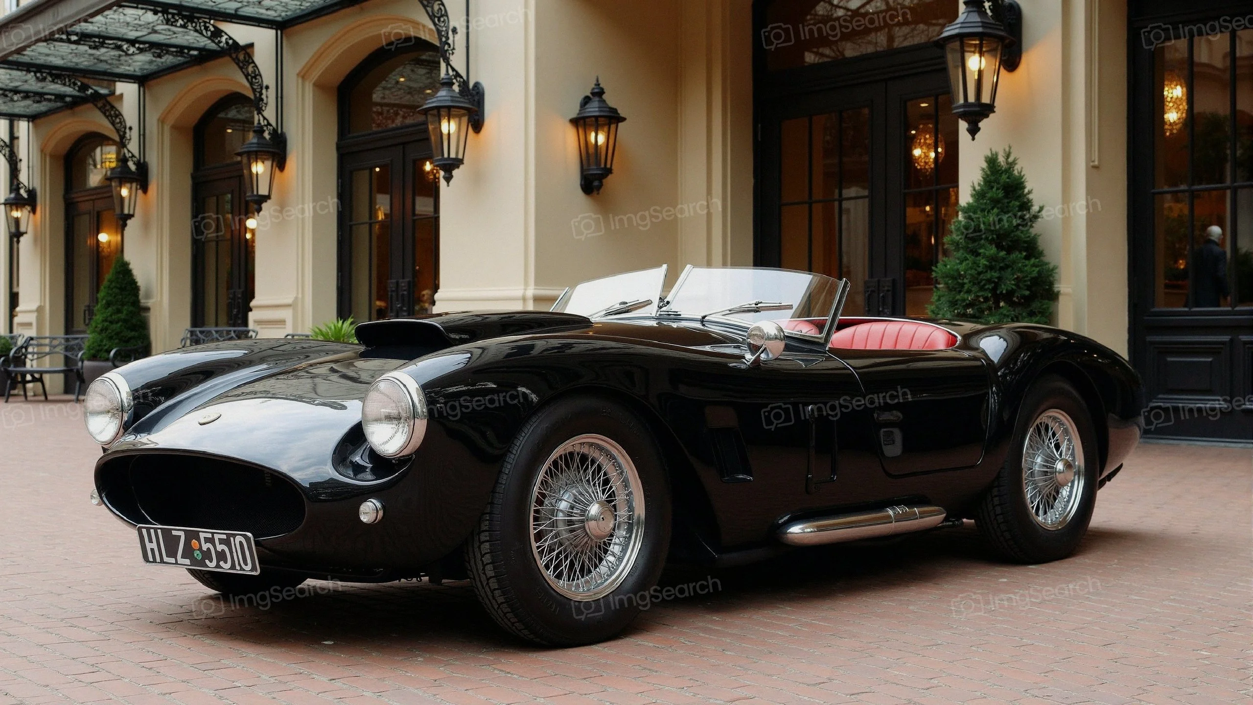 A classic black sports car with red leather interior parked in front of an elegant building.
