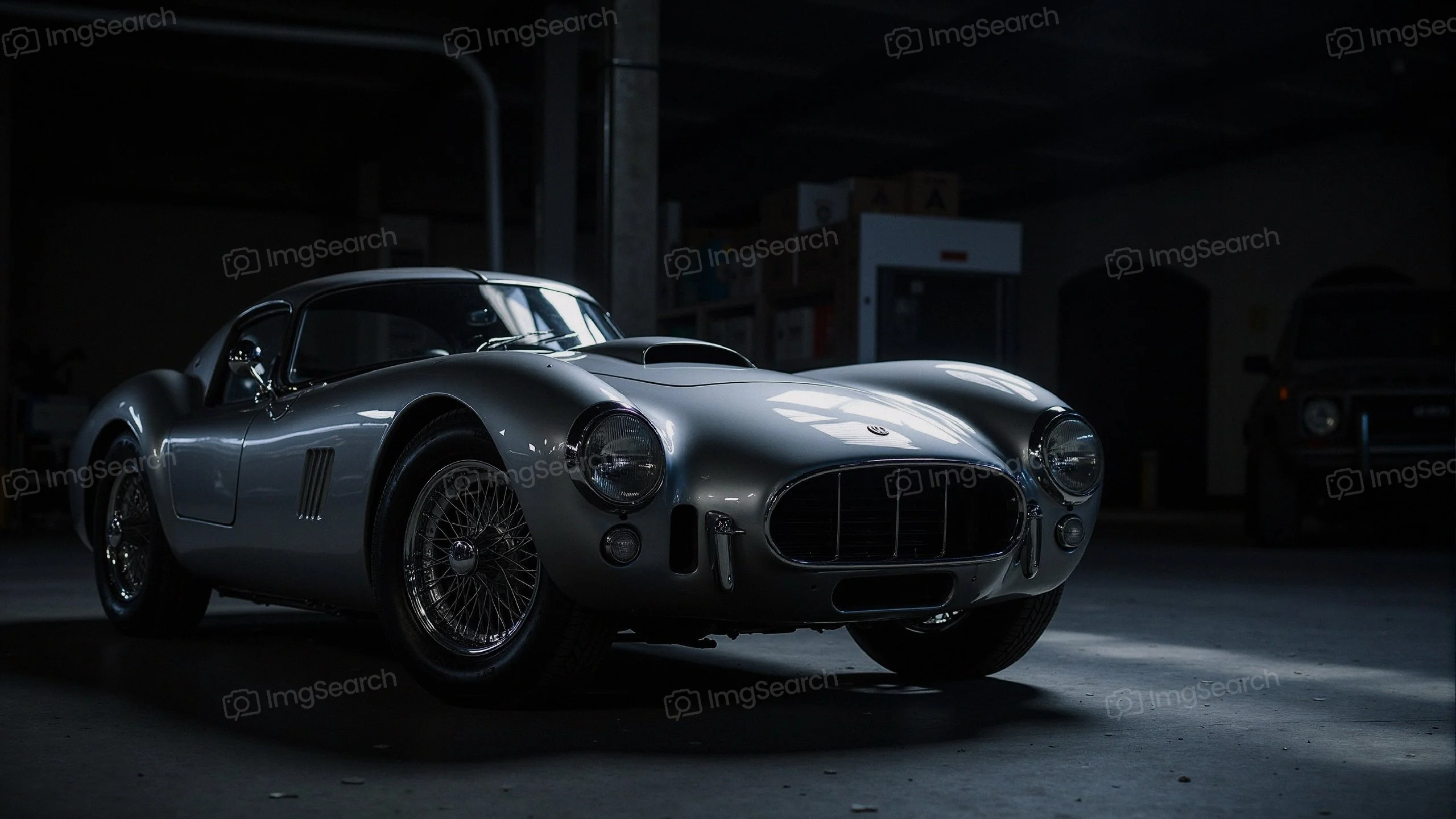 A classic silver sports car with wire-spoke wheels parked in a dimly lit garage.