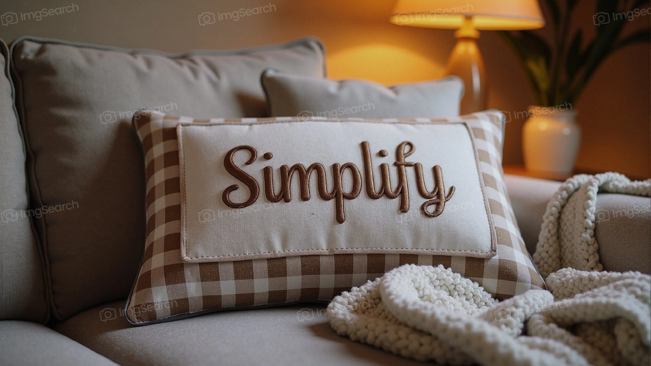 A cozy living room scene with a decorative pillow that says 'Simplify', a textured blanket, warm lighting.