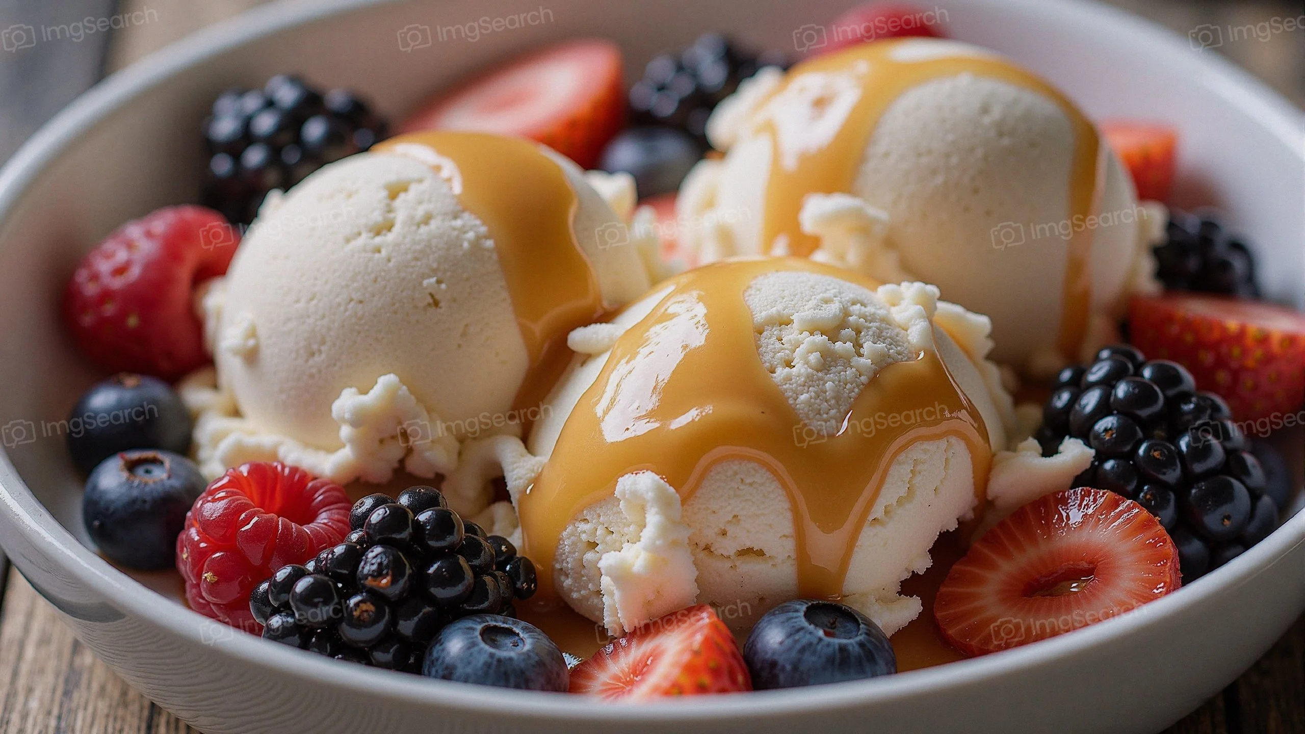 A bowl of vanilla ice cream topped with caramel sauce surrounded by fresh berries.