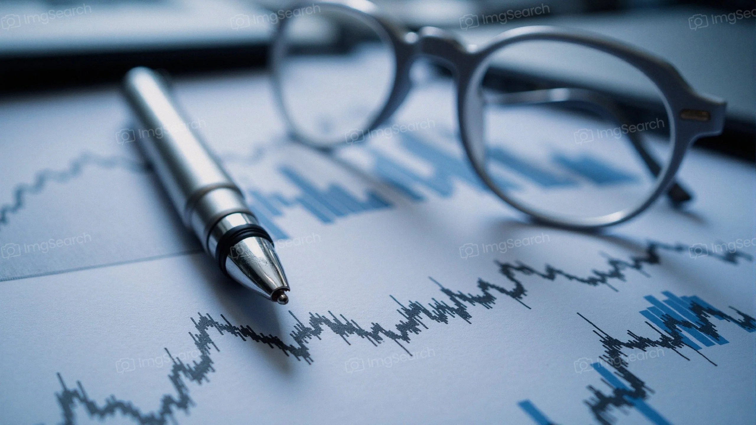 Close-up of a financial chart with a silver pen eyeglasses.