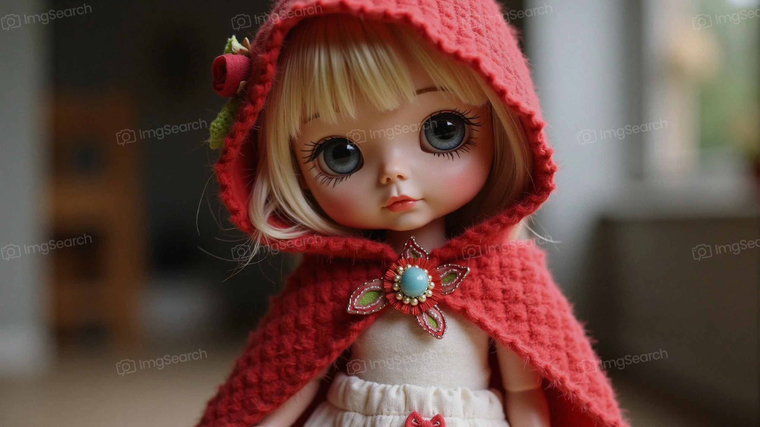 A doll wearing a red hooded cloak posing indoors.