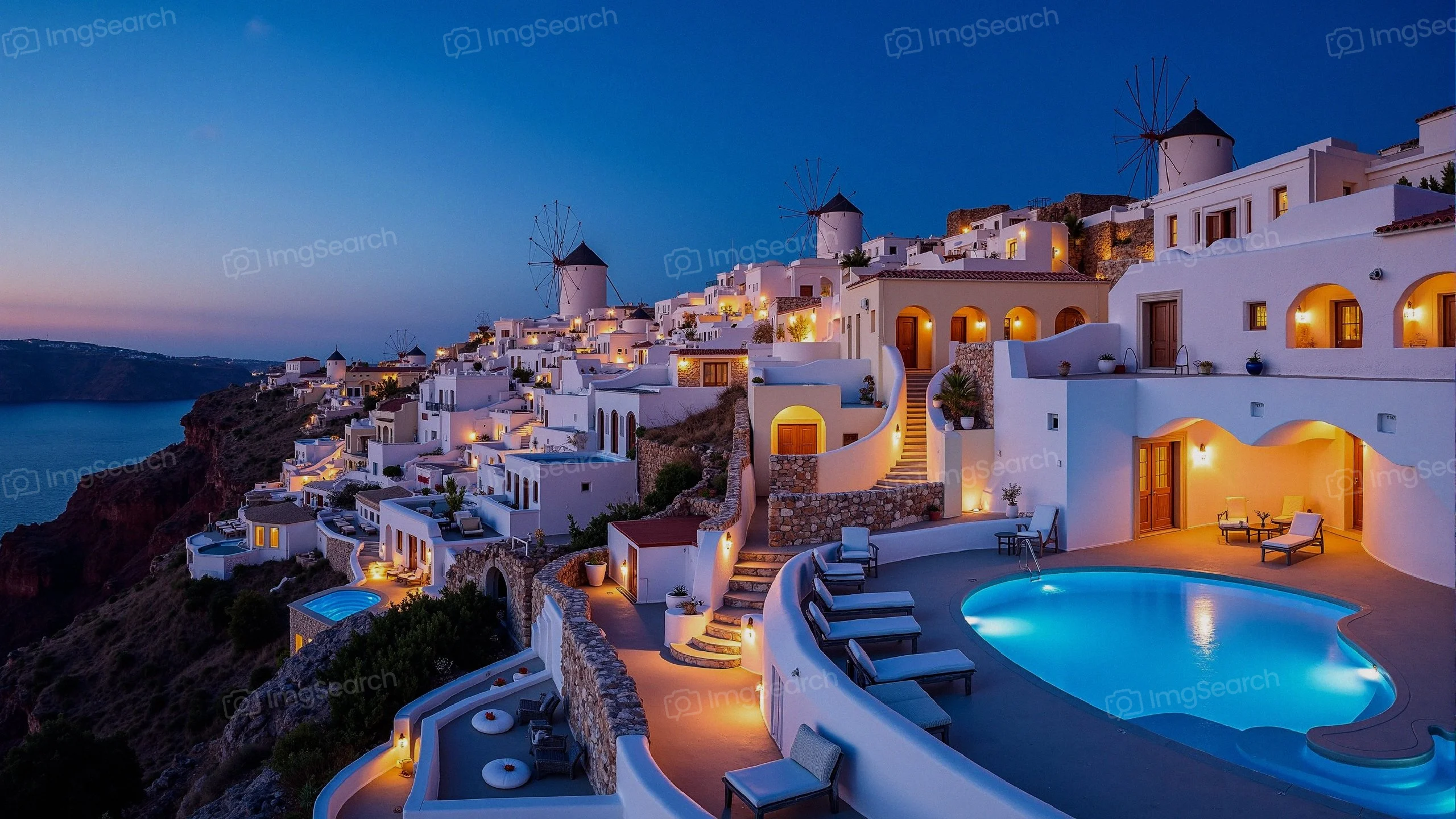 A picturesque view of Santorini at dusk with illuminated buildings a swimming pool.