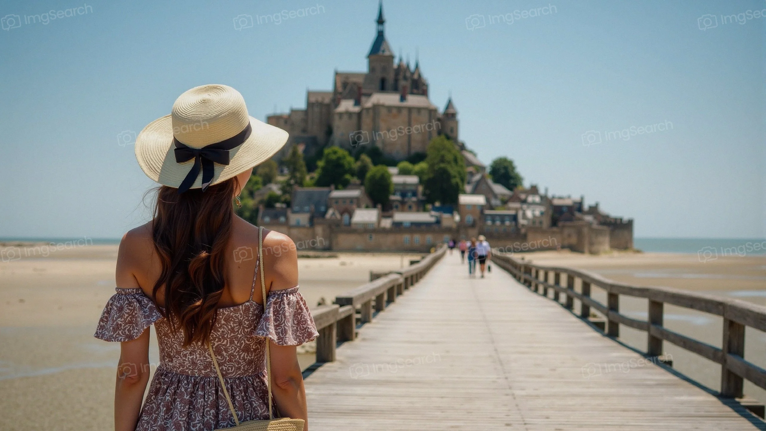 A woman with a straw hat views Mont Saint-Michel from a wooden walkway