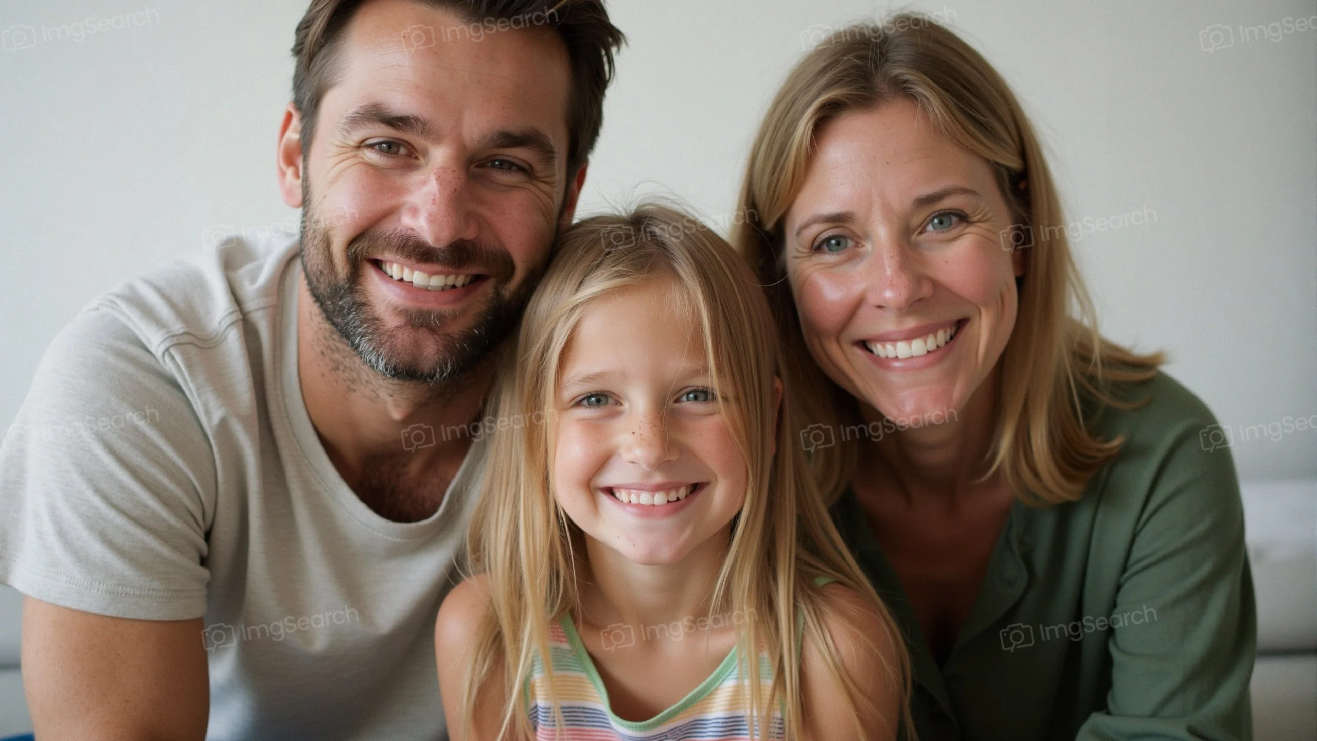 A cheerful family consisting of a father, mother, and daughter smiling at the camera.