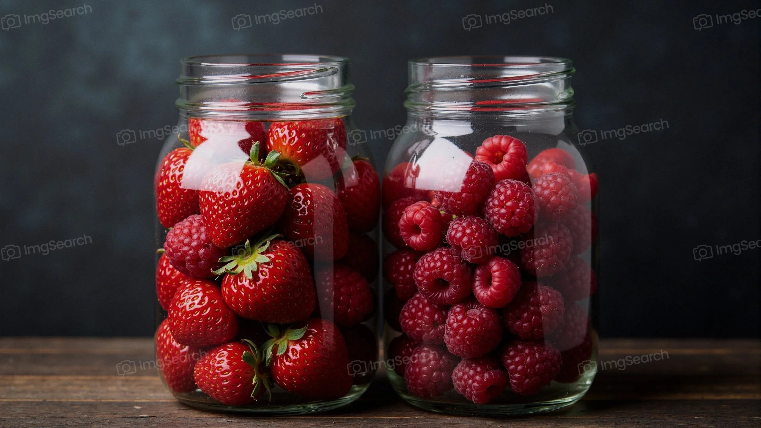 Two glass jars filled with strawberries raspberries against a dark background.