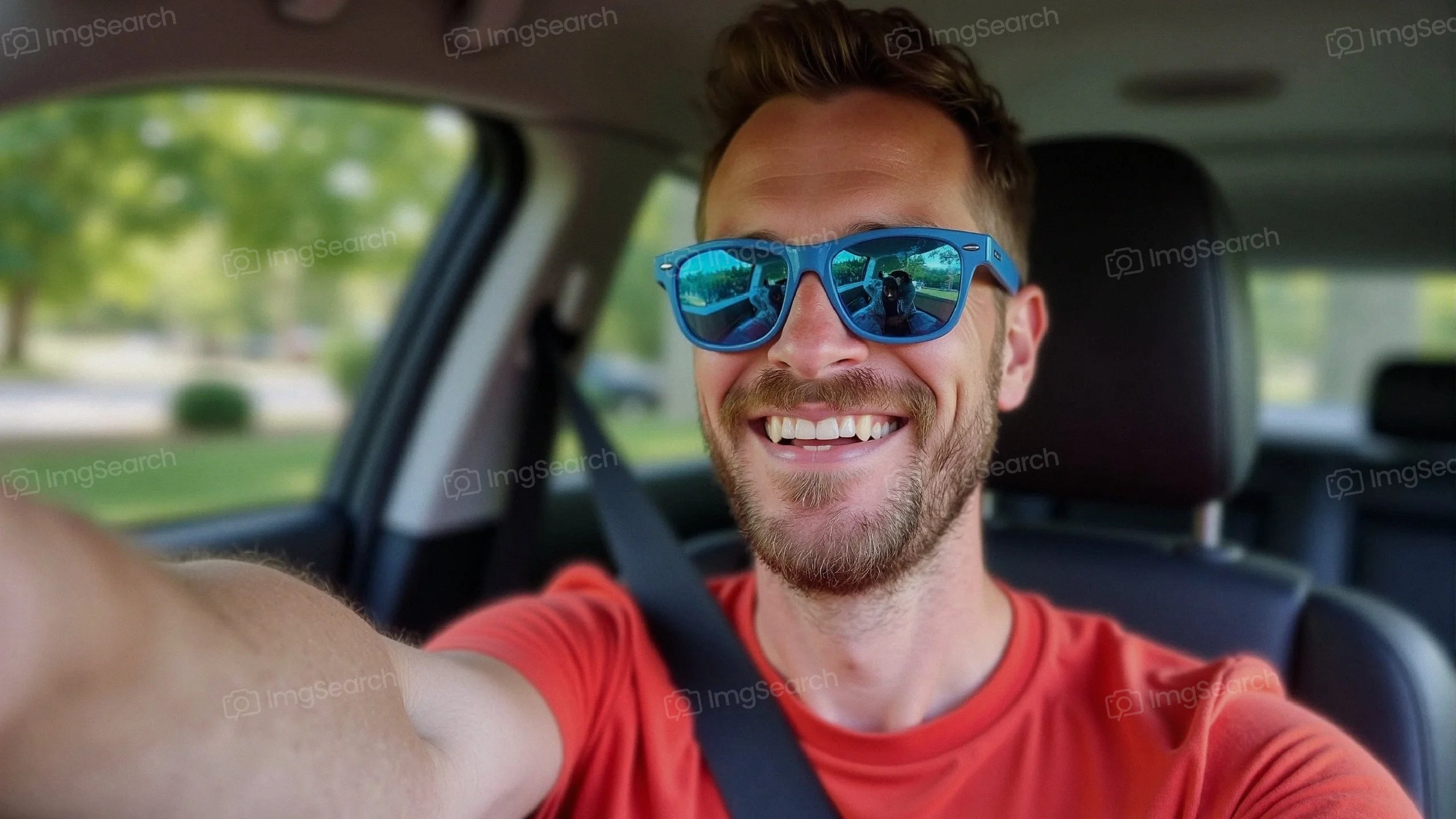 A young man with sunglasses smiling while taking a selfie in a car