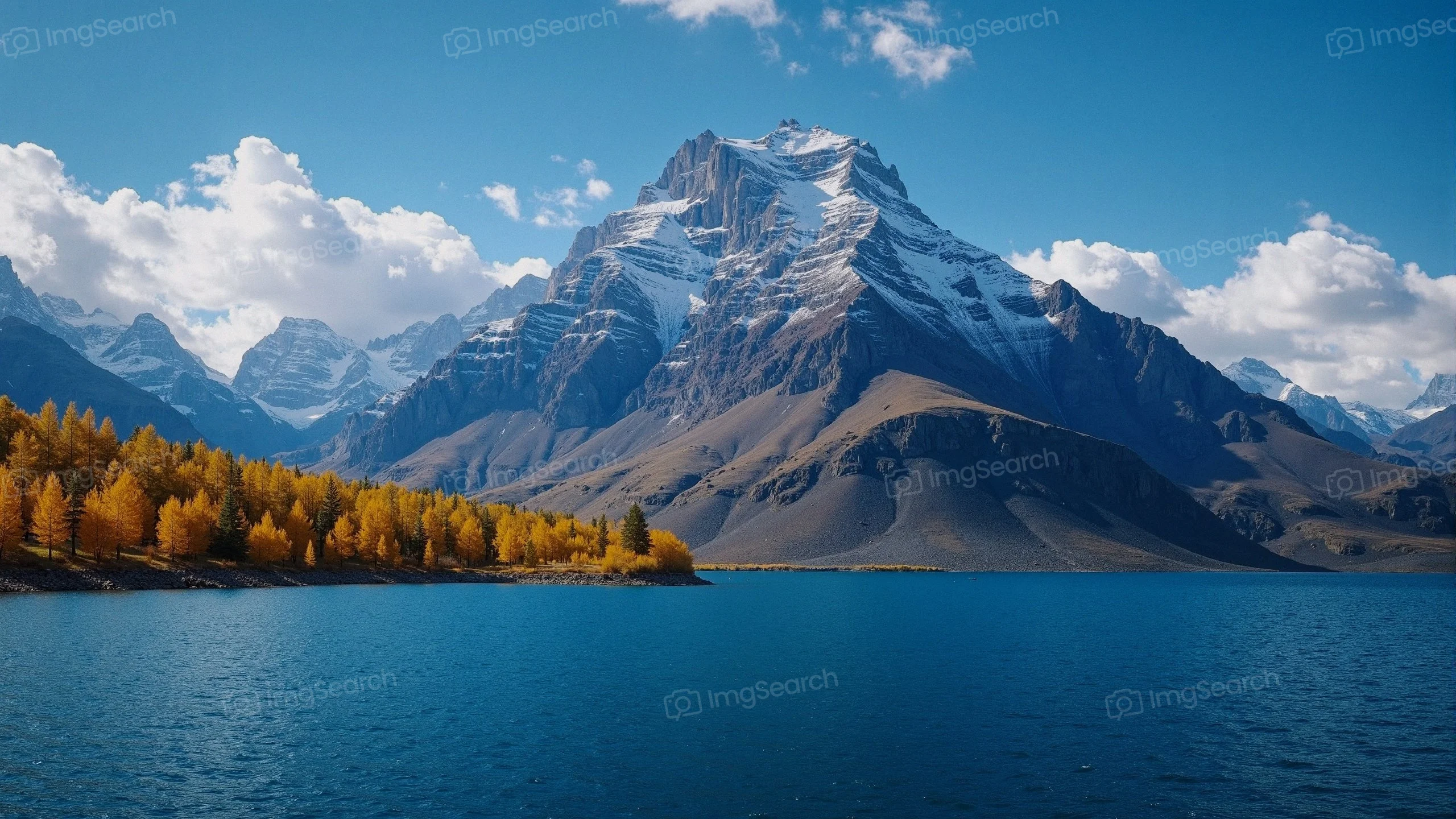 A scenic view of mountains with autumn foliage reflecting in a lake under a blue sky