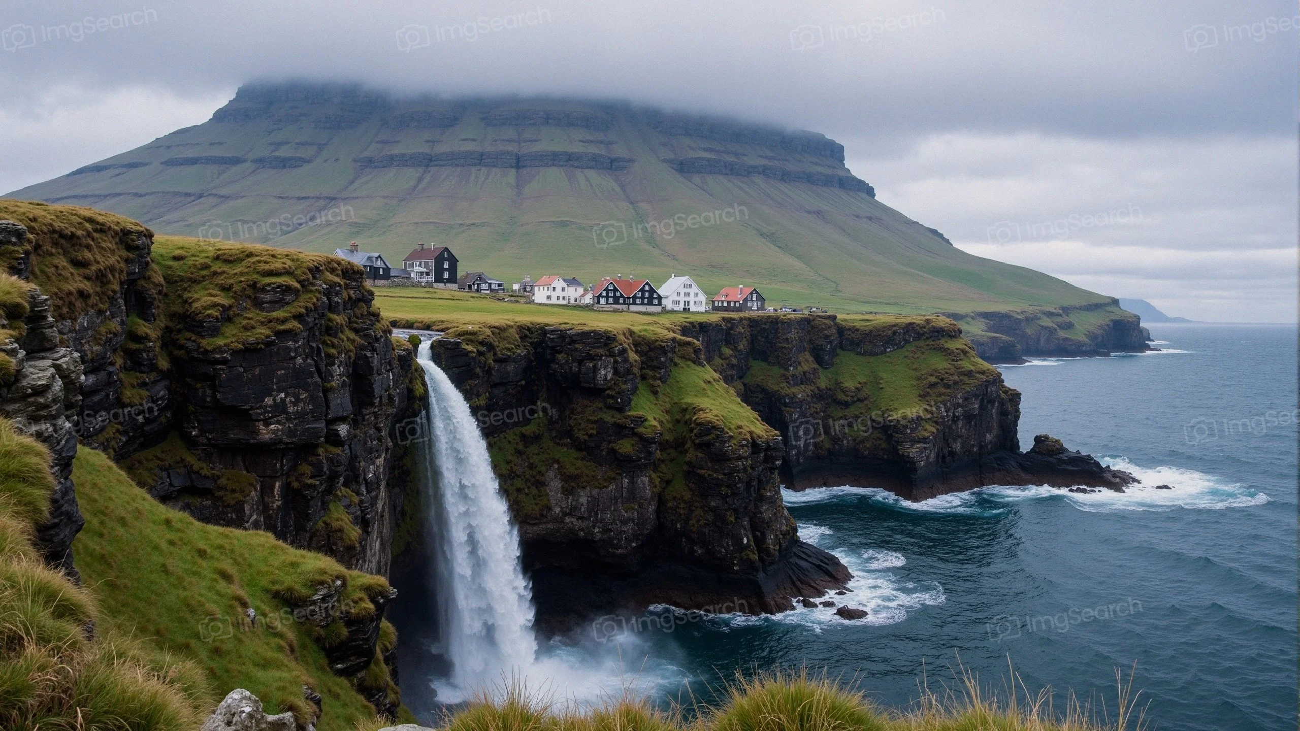 Scenic view of a waterfall falling from cliffs into the ocean in the Faroe Islands with a village in the background