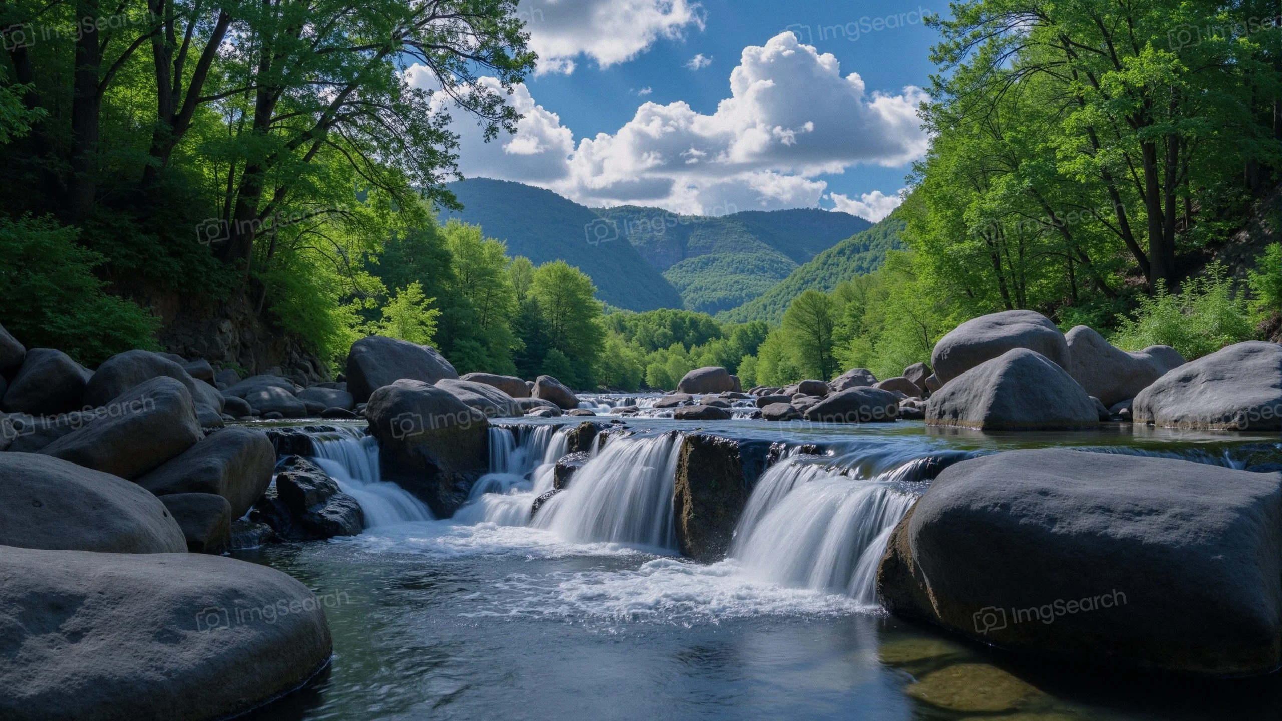 A mountain stream with a waterfall surrounded by lush greenery a clear blue sky.