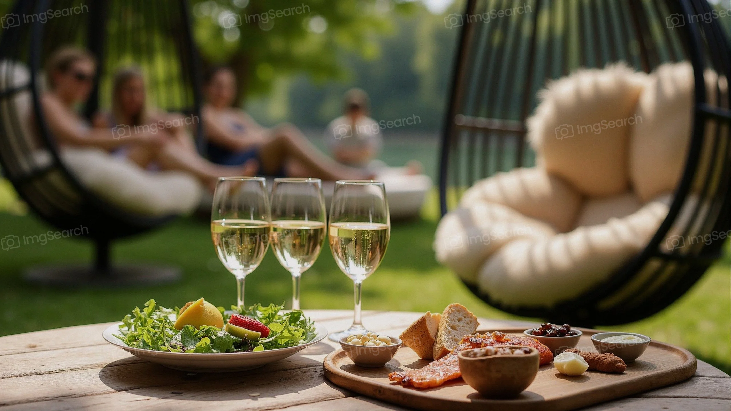 A picnic table with gourmet food sparkling wine glasses in an outdoor setting with friends in the background.