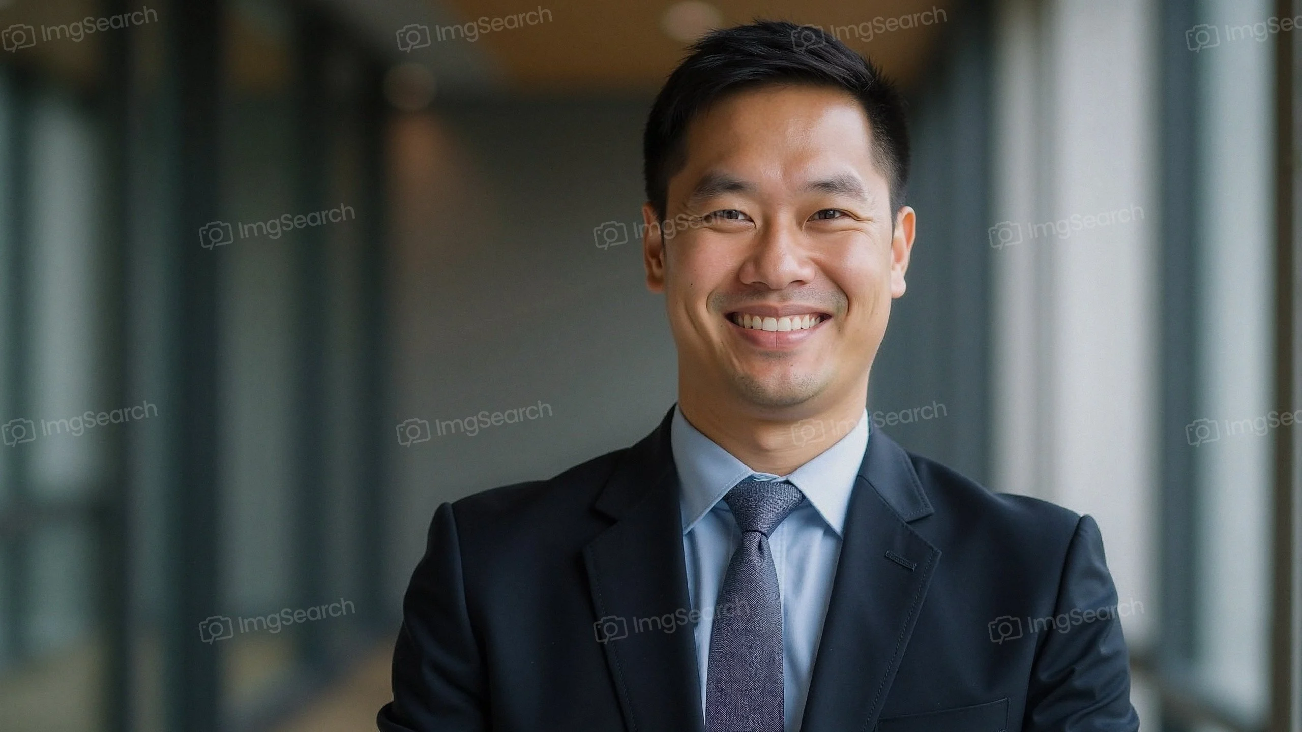 A professional man smiling in a business suit in an office setting.