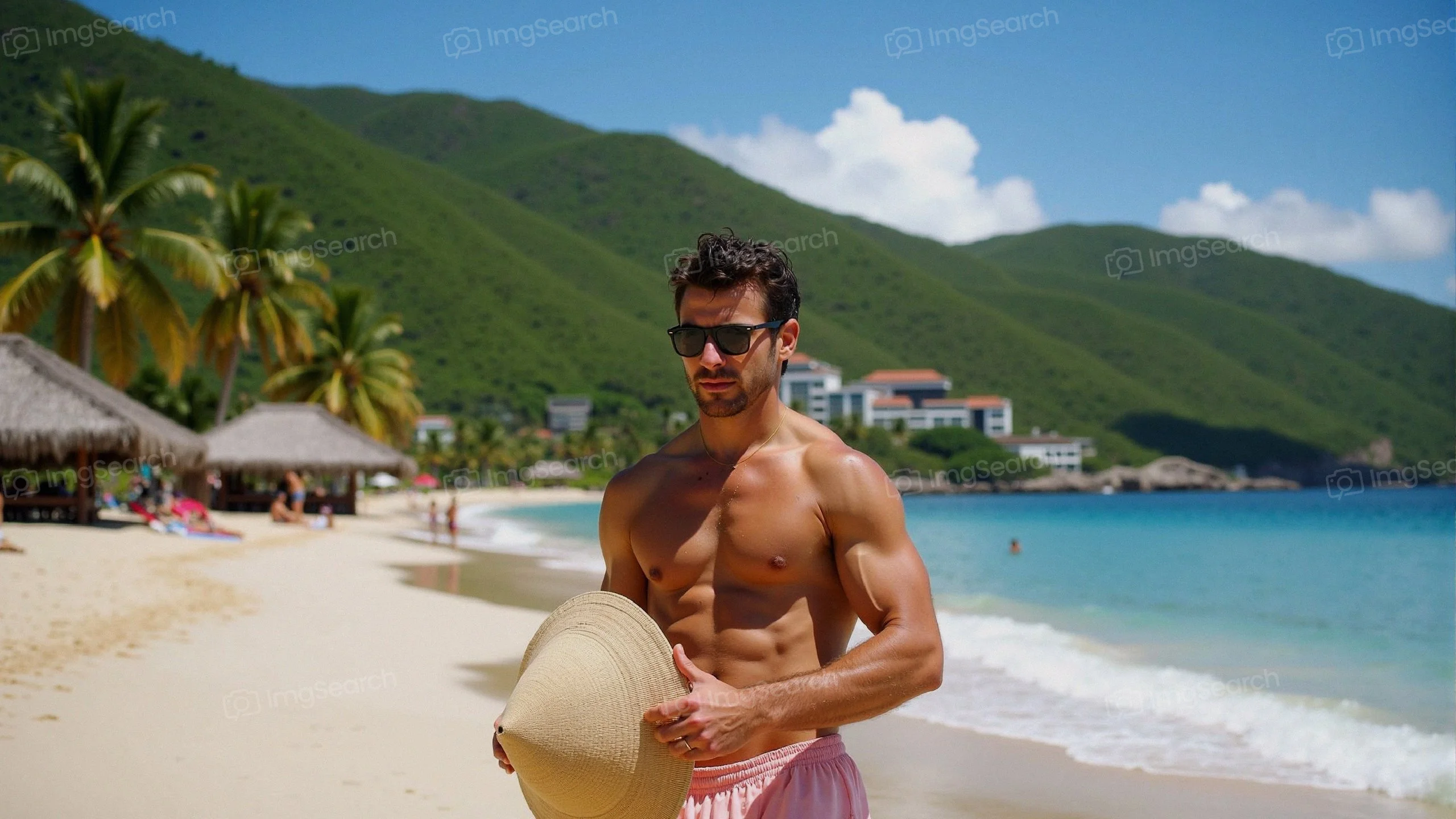 A fit man in sunglasses holding a straw hat on a tropical beach
