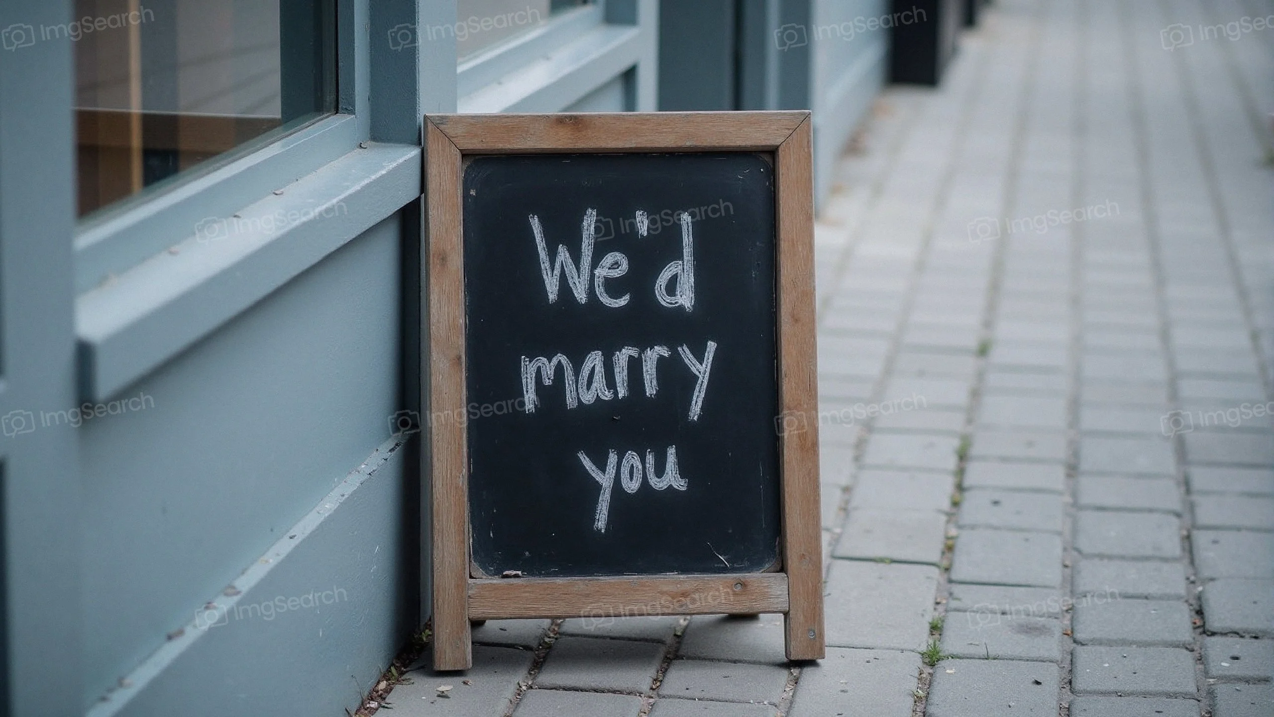 A wooden signboard that reads 'We'd marry you' in white chalk on a blue background.