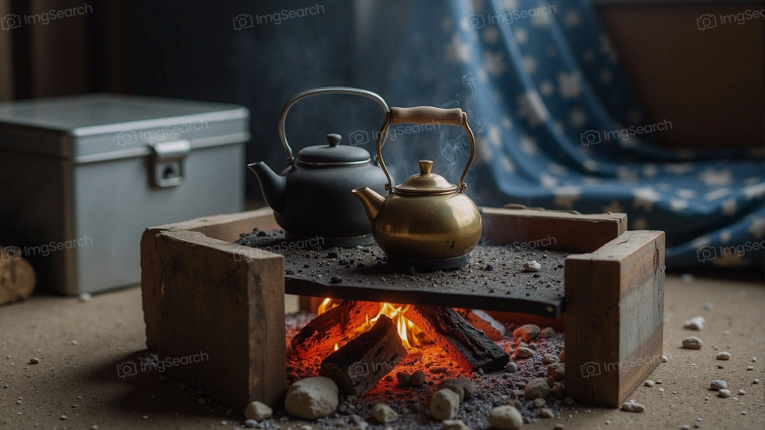 Two teapots, one black one gold, placed on a stone over a campfire with glowing embers.