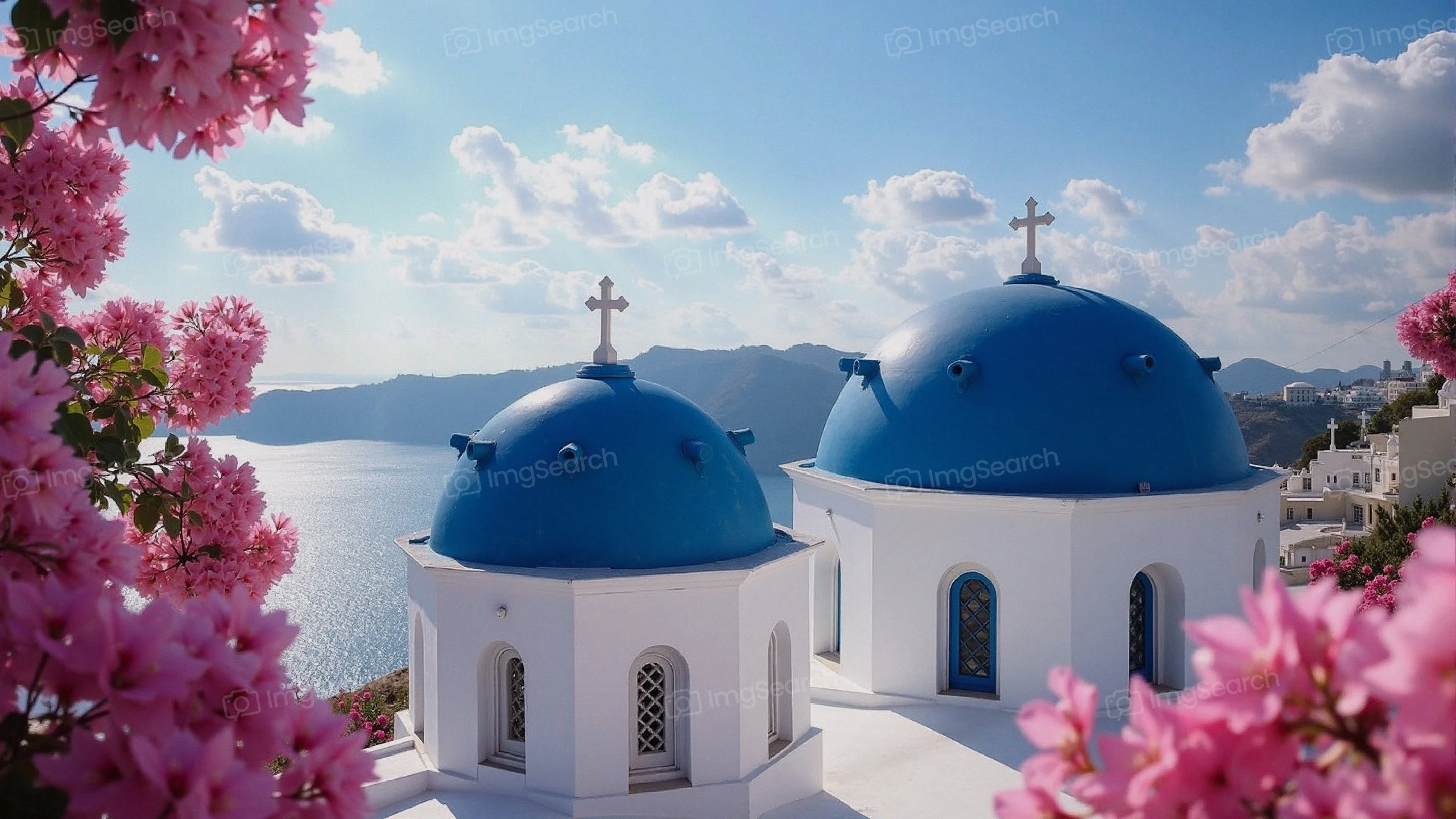 A view of Santorini's iconic blue-domed churches surrounded by pink bougainvillea flowers the Aegean Sea.