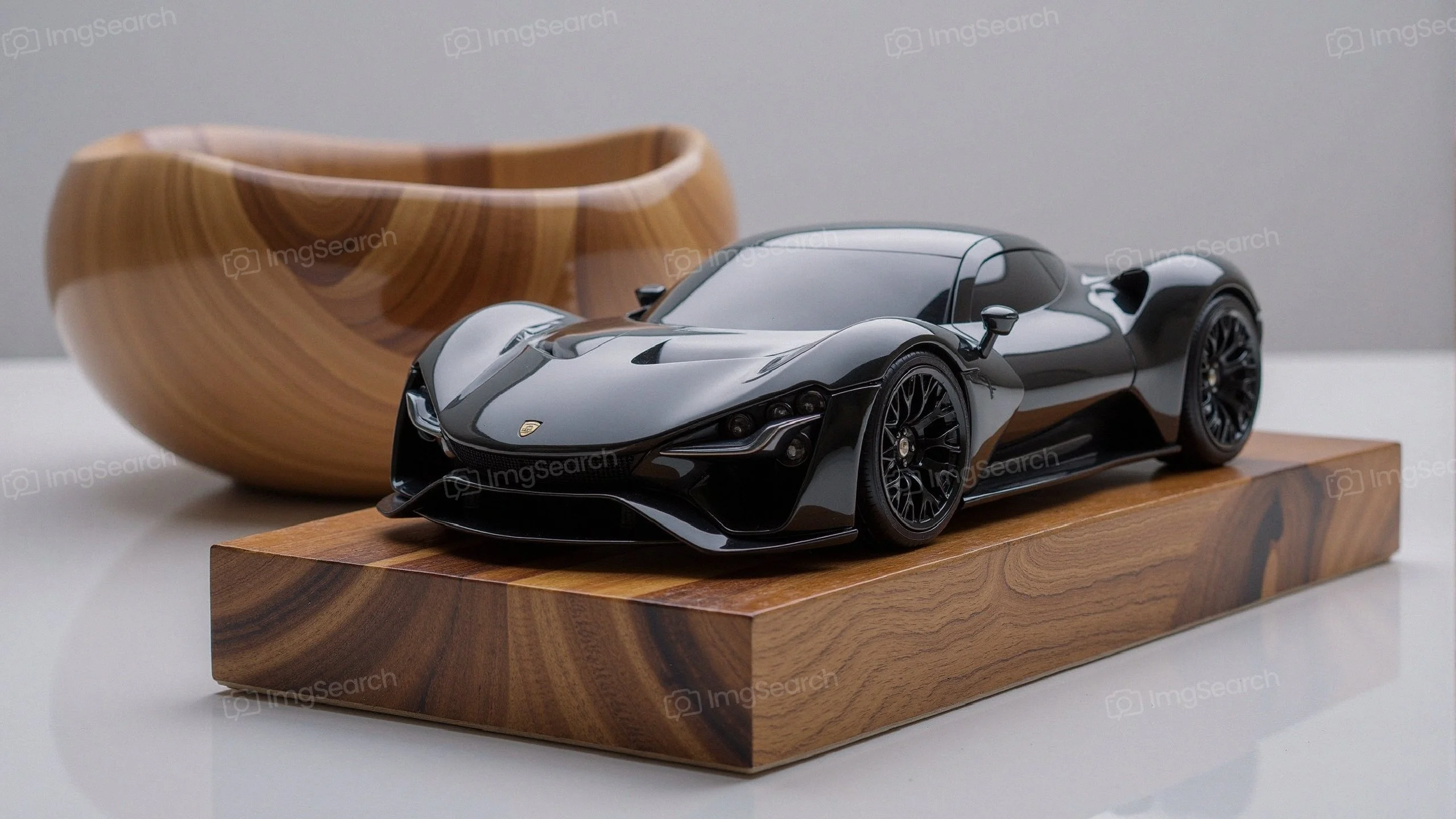 A sleek black sports car model on an elegant wooden base with a wooden bowl in the background.