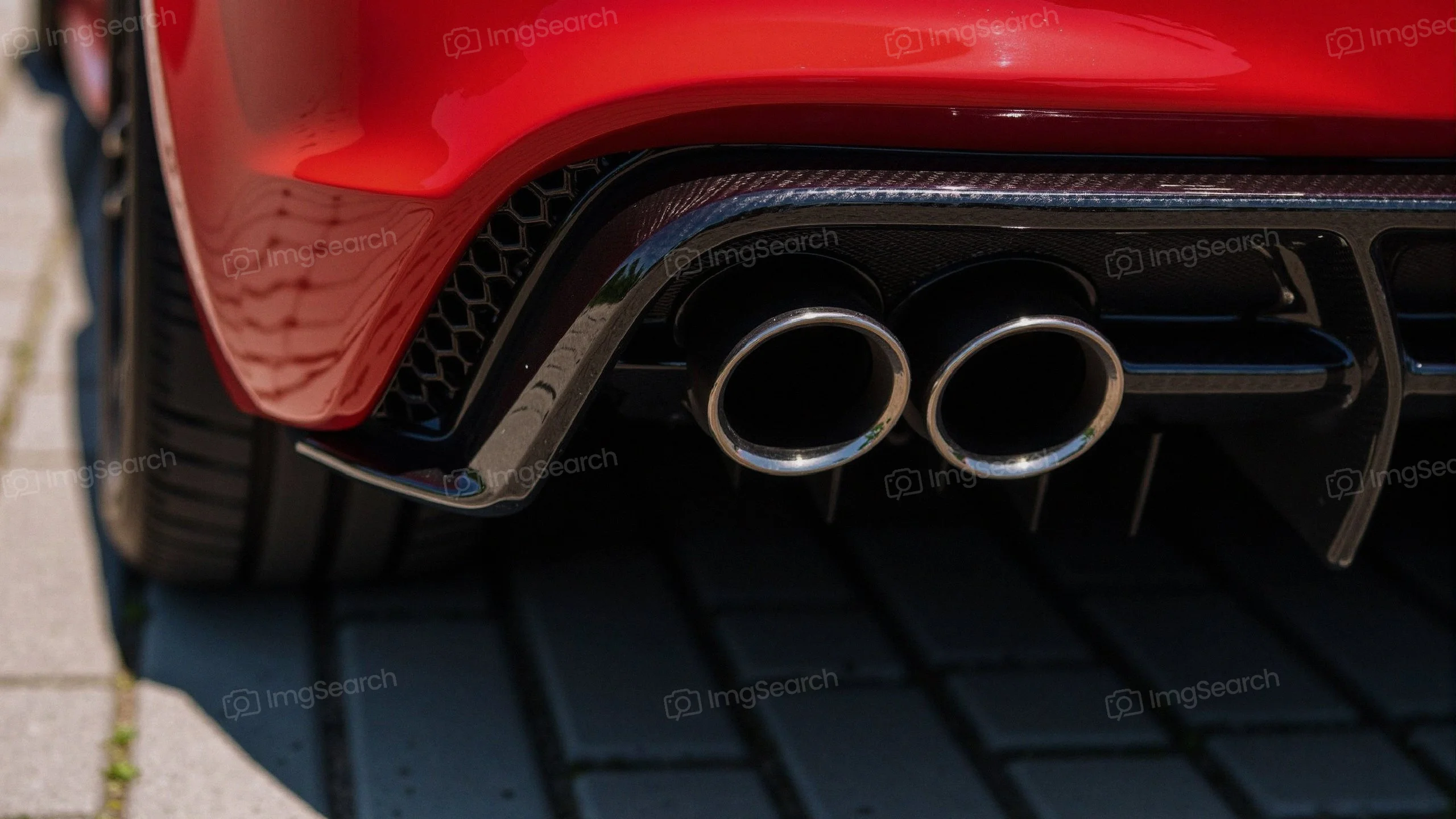 Close-up of the dual exhaust system of a red sportscar with carbon fiber accents