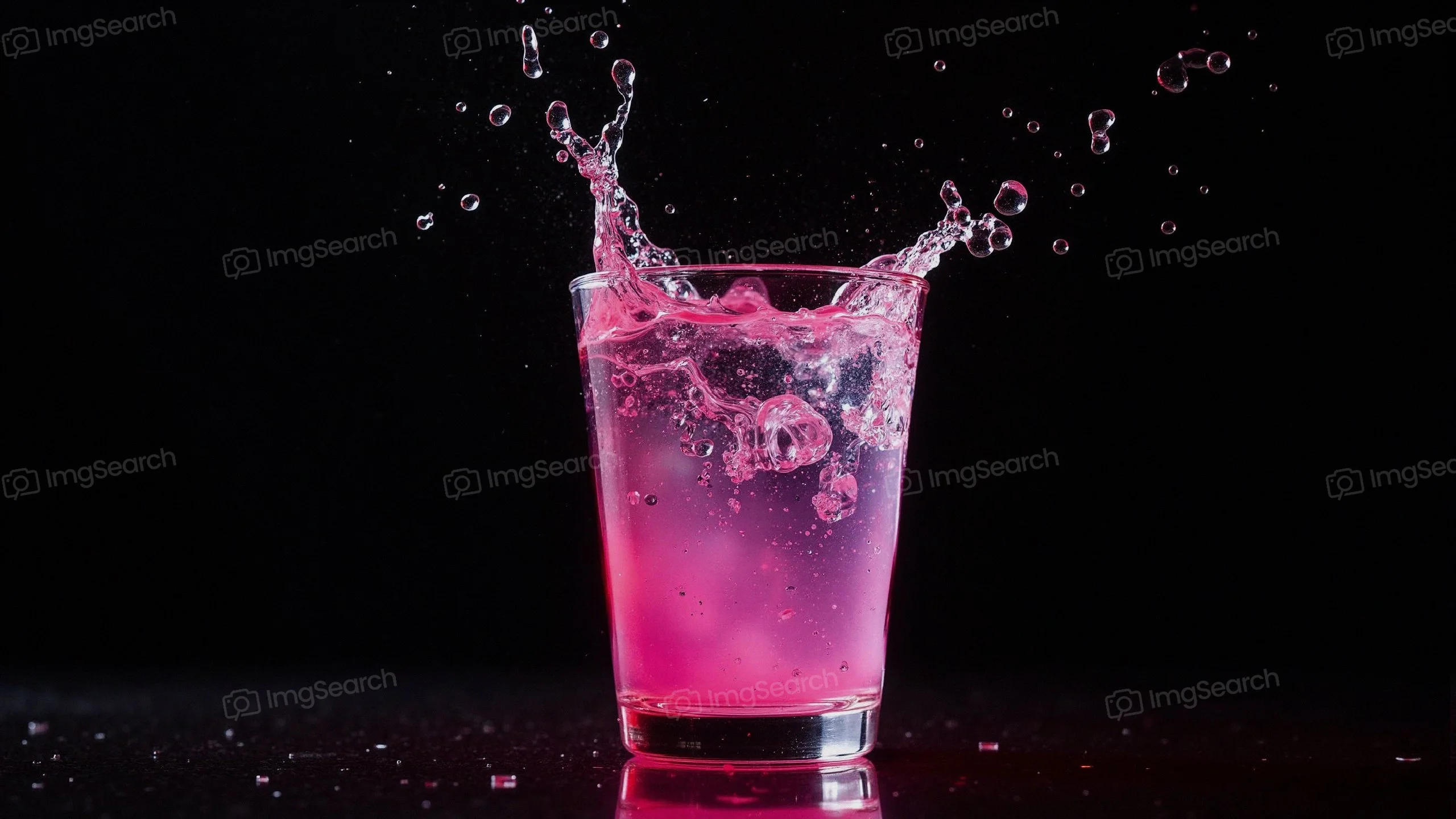 A glass filled with a pink drink splashing against a dark background