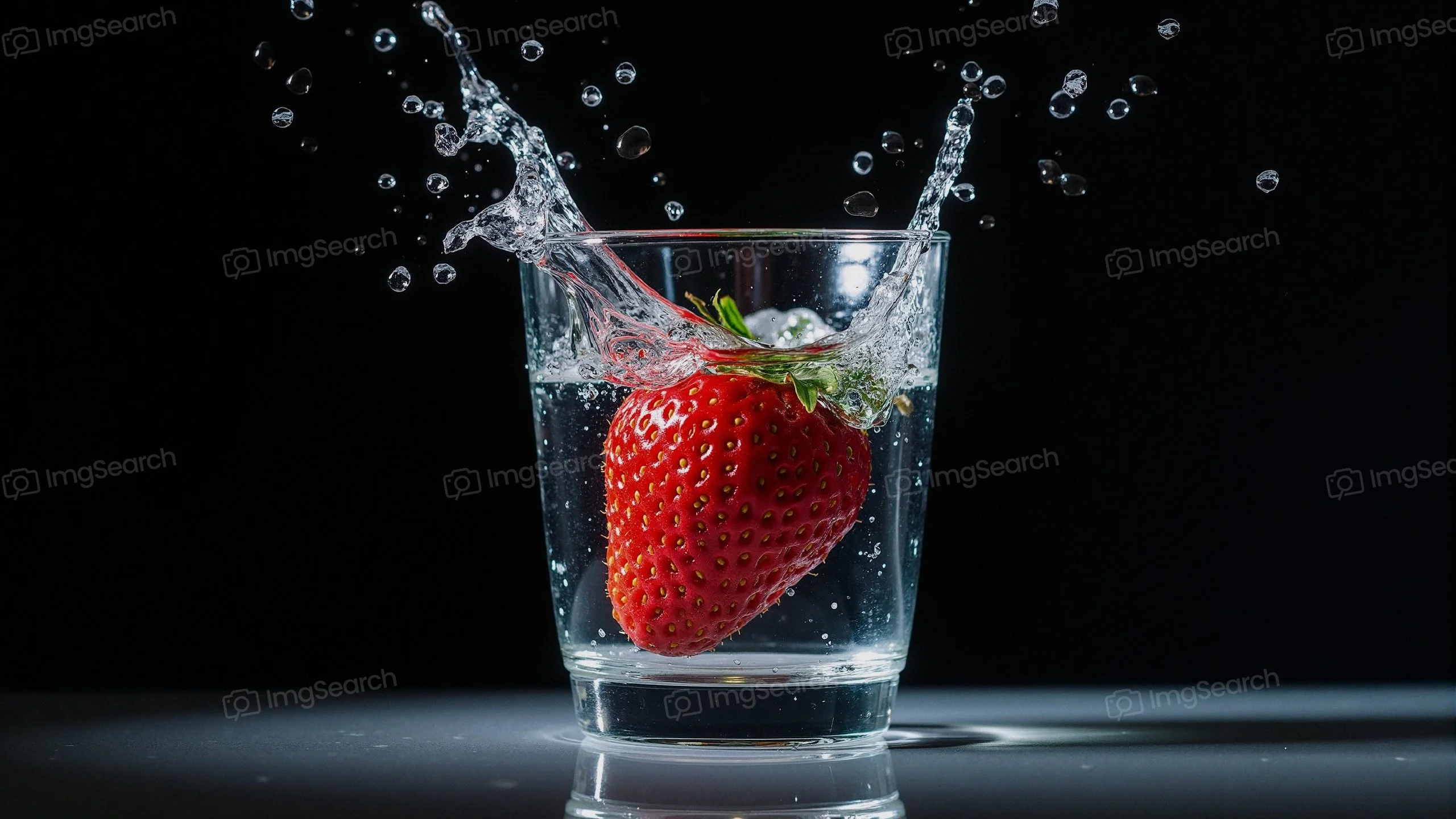 A strawberry splashing into a glass of water with droplets bursting around