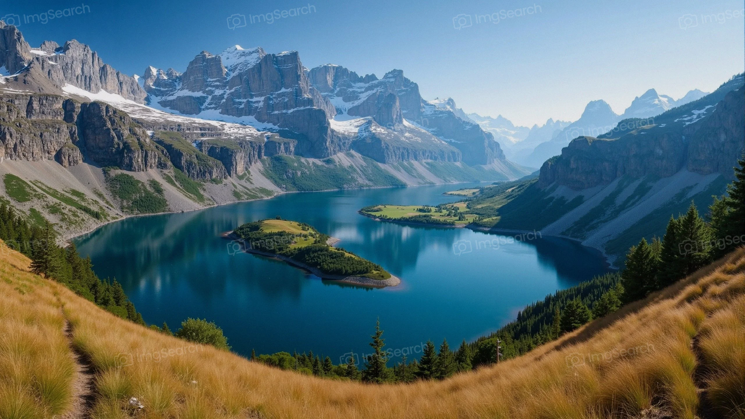 A breathtaking view of mountains surrounding a calm lake with lush green islands foreground grass.