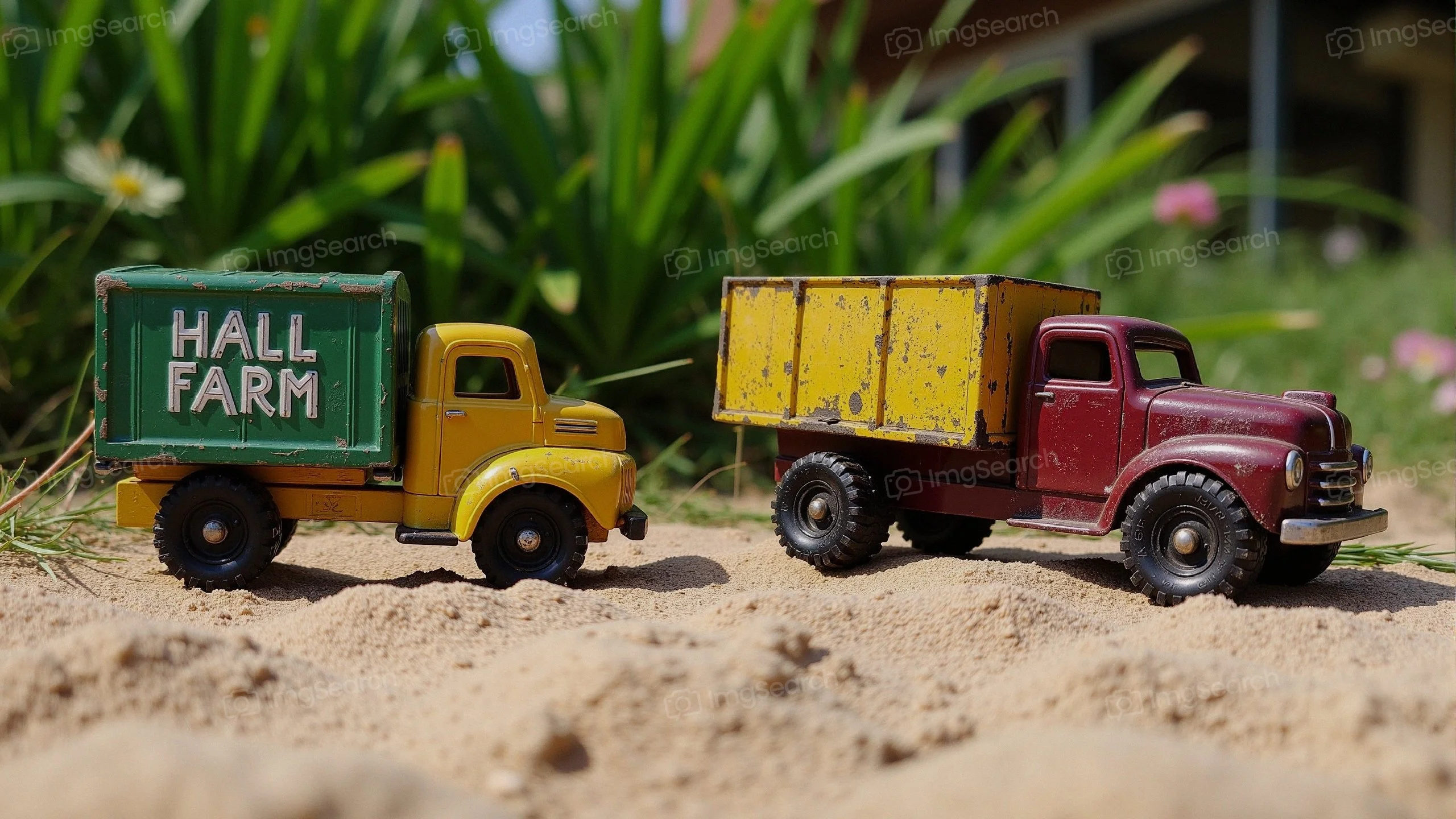 Two vintage toy trucks on sand with green grass