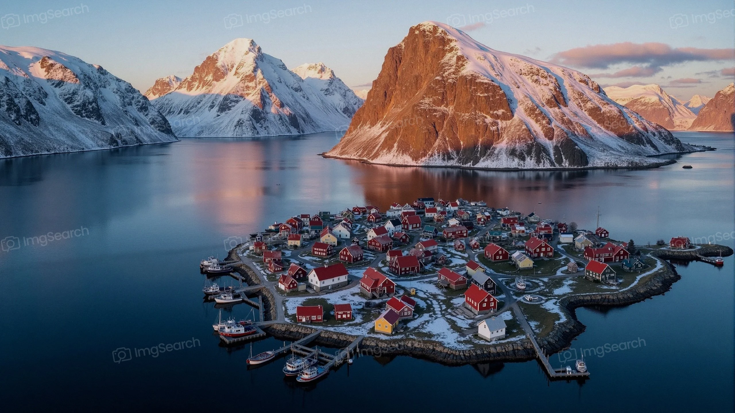 Aerial view of a snowy coastal village with colorful houses surrounding mountains.